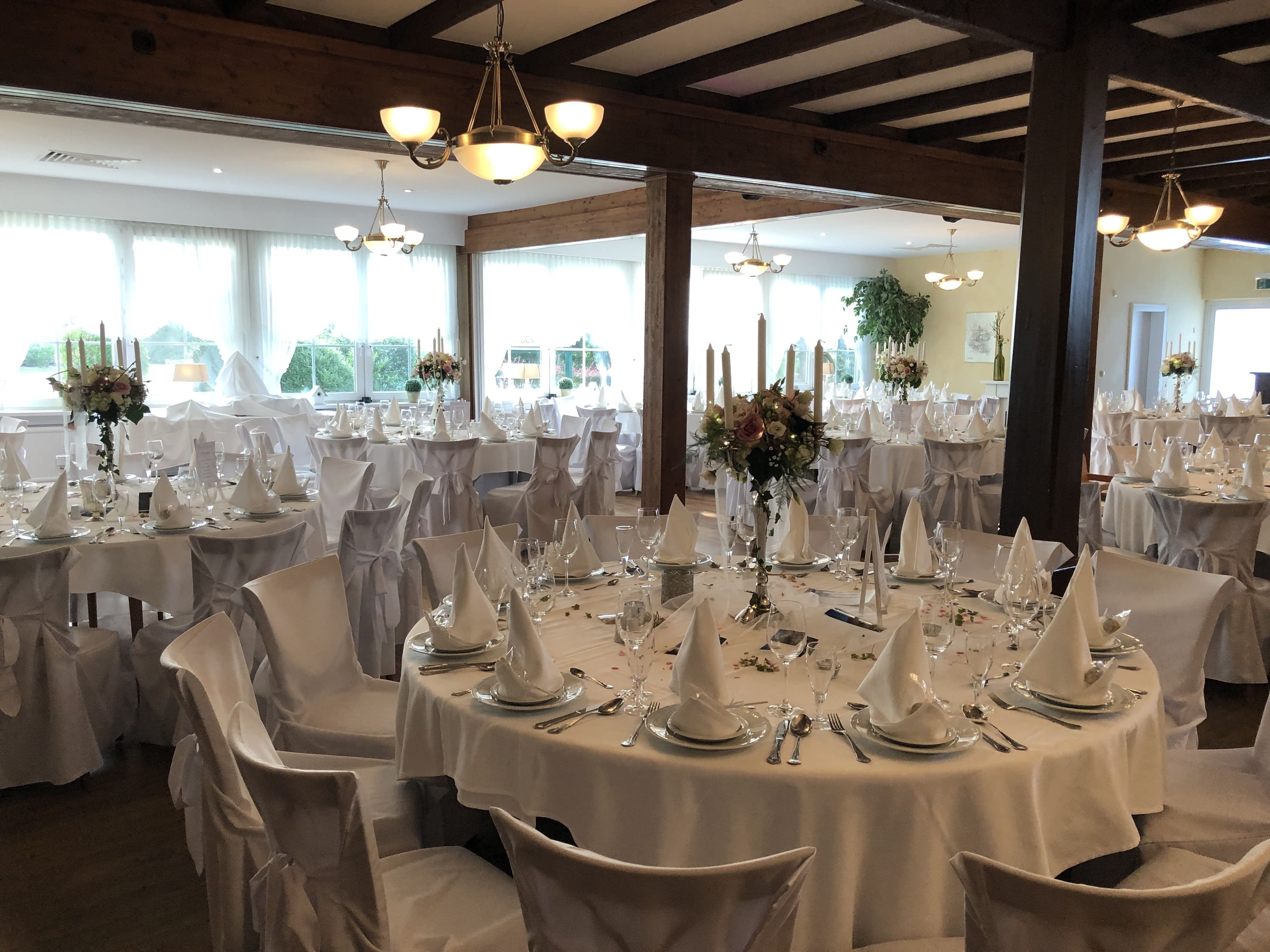 Veranstaltungssaal mit festlich eidgedeckten Tischen in weiß.